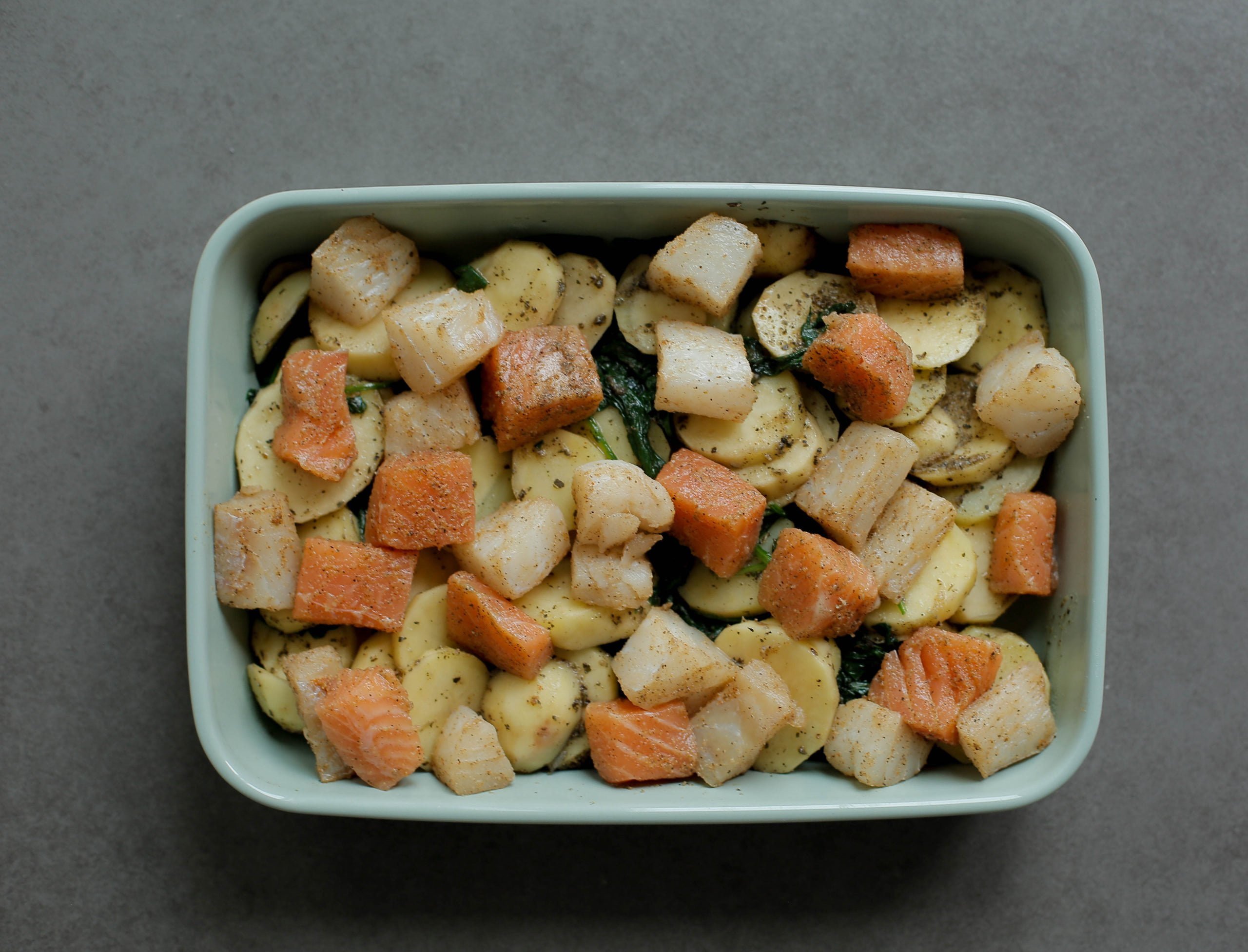 Vismengsel over het aardappelmengsel in een ovenschaal