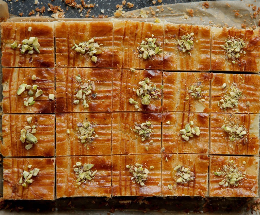 Snijd de pistache boterkoek in stukken en garneer met gemalen pistachenoten.