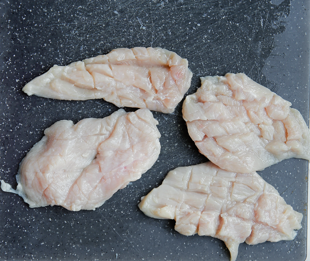 Snijd de kipfilet in 4 stukken. Snijd inkepingen in de lengte en breedte van de kip.