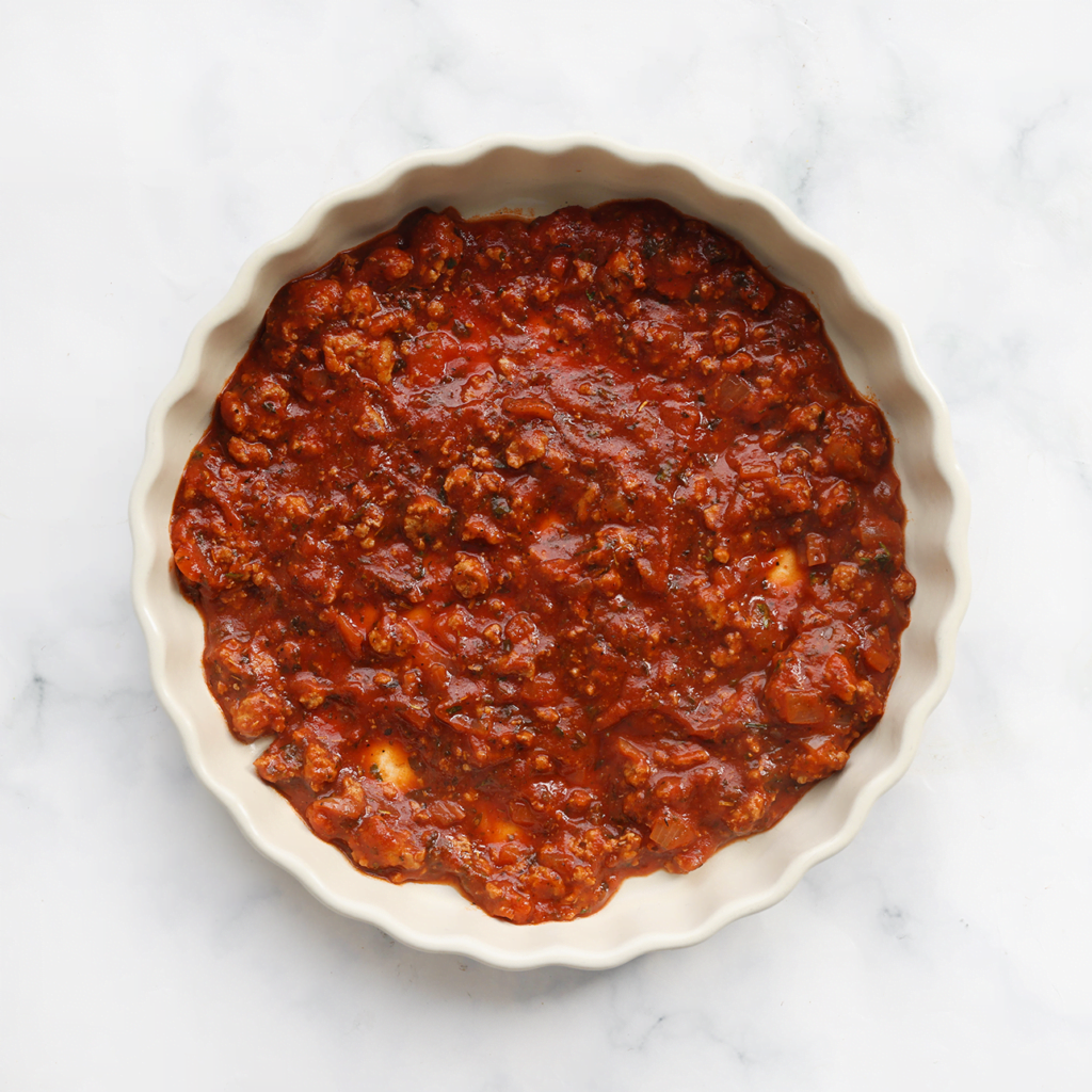Verdeel een laagje tomatensaus over de ovenschaal. Doe de rest van het gehaktmengsel in een spuitzak.
