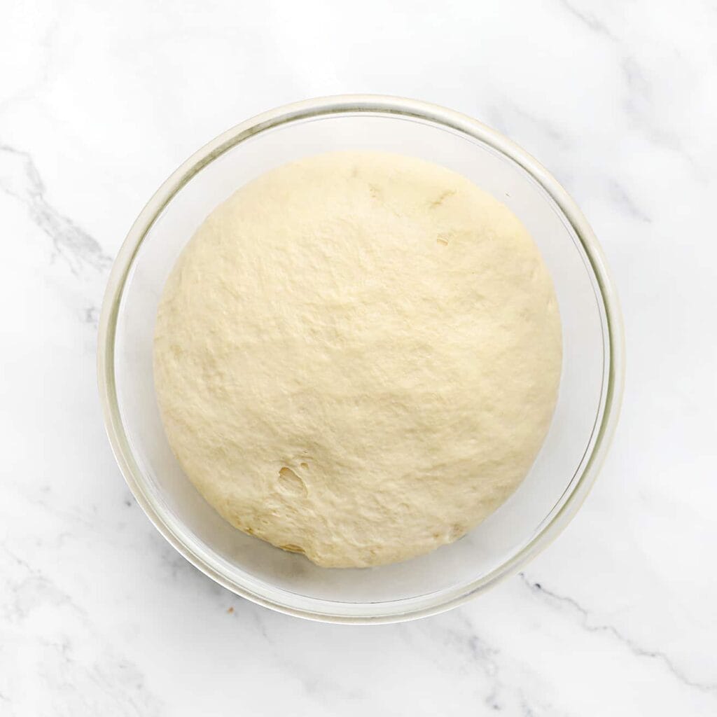 Dek het deeg af en laat het 1 uur rijzen op een warme plek in huis, of totdat het deeg in omvang is verdubbeld.