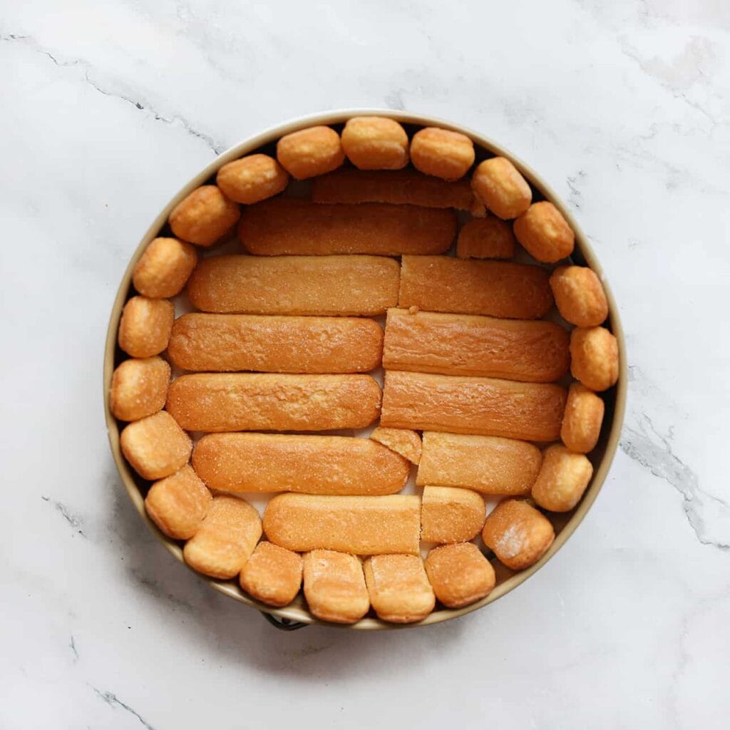 Verdeel de lange vingers langs de randen van de springvorm en daarna over de bodem.