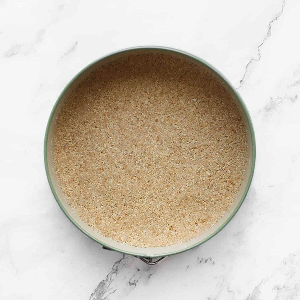 Neem een springvorm of bakvorm en leg er een vel bakpapier in. Verdeel het koekjesdeeg gelijkmatig over de bodem en druk het stevig aan met behulp van de onderkant van een lepel. Plaats de bakvorm met het koekjesdeeg kort in de koelkast.