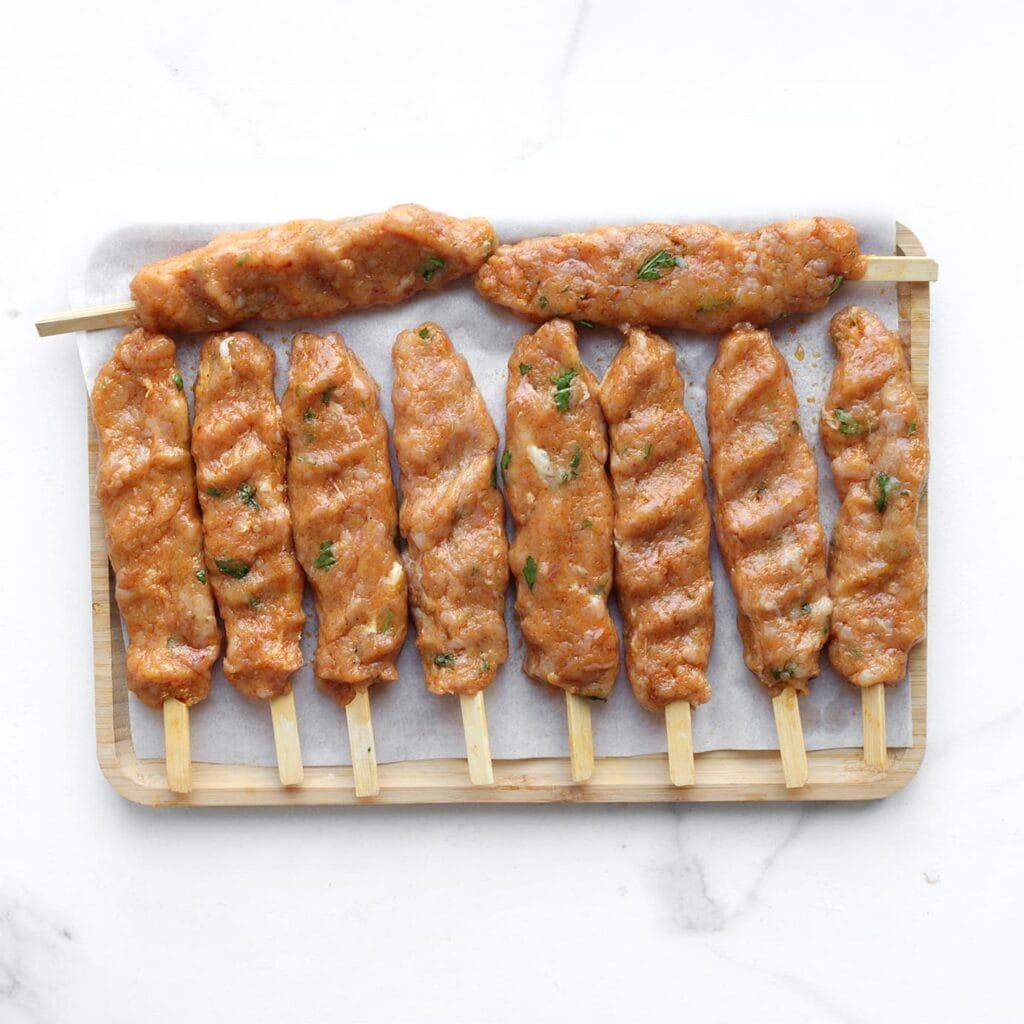 Neem een portie van het kipgehakt en vorm deze in je handpalm tot een platte schijf. Leg een houten stokje in het midden en vouw het gehakt eromheen. Druk stevig aan zodat het goed blijft zitten. Herhaal tot al het gehakt op is.