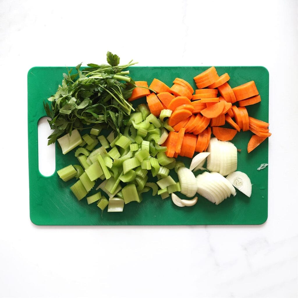 Schil en snijd de wortel in blokjes. Snijd de selderij in stukken. Pel en snijd de gele ui in plakjes. Snijd de peterselie.