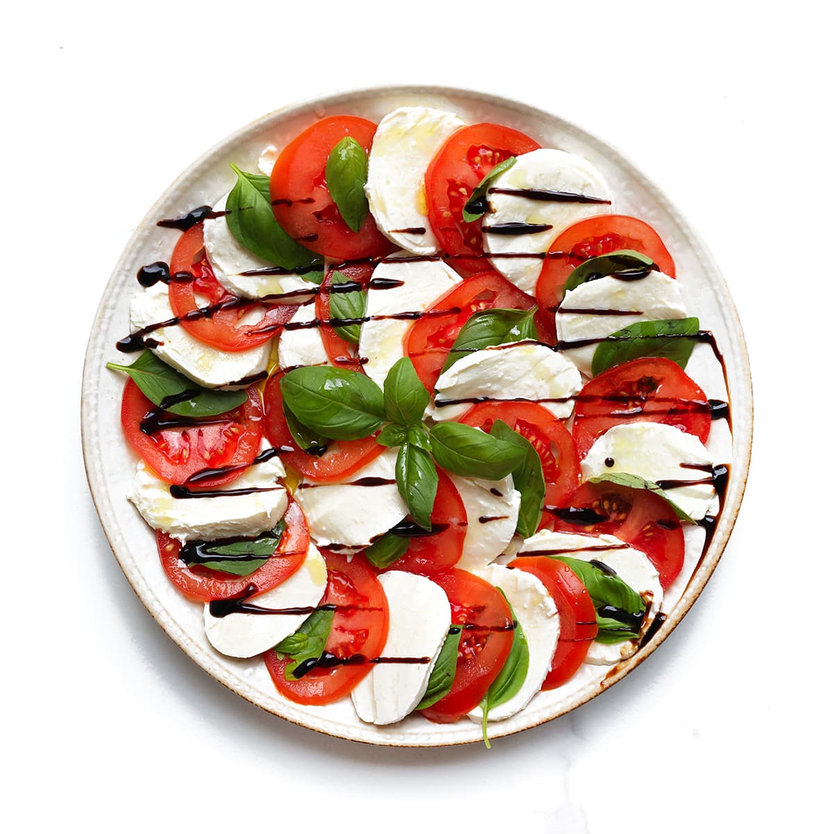 Salade caprese op een bord met basilicum en geroosterde pijnboompitten