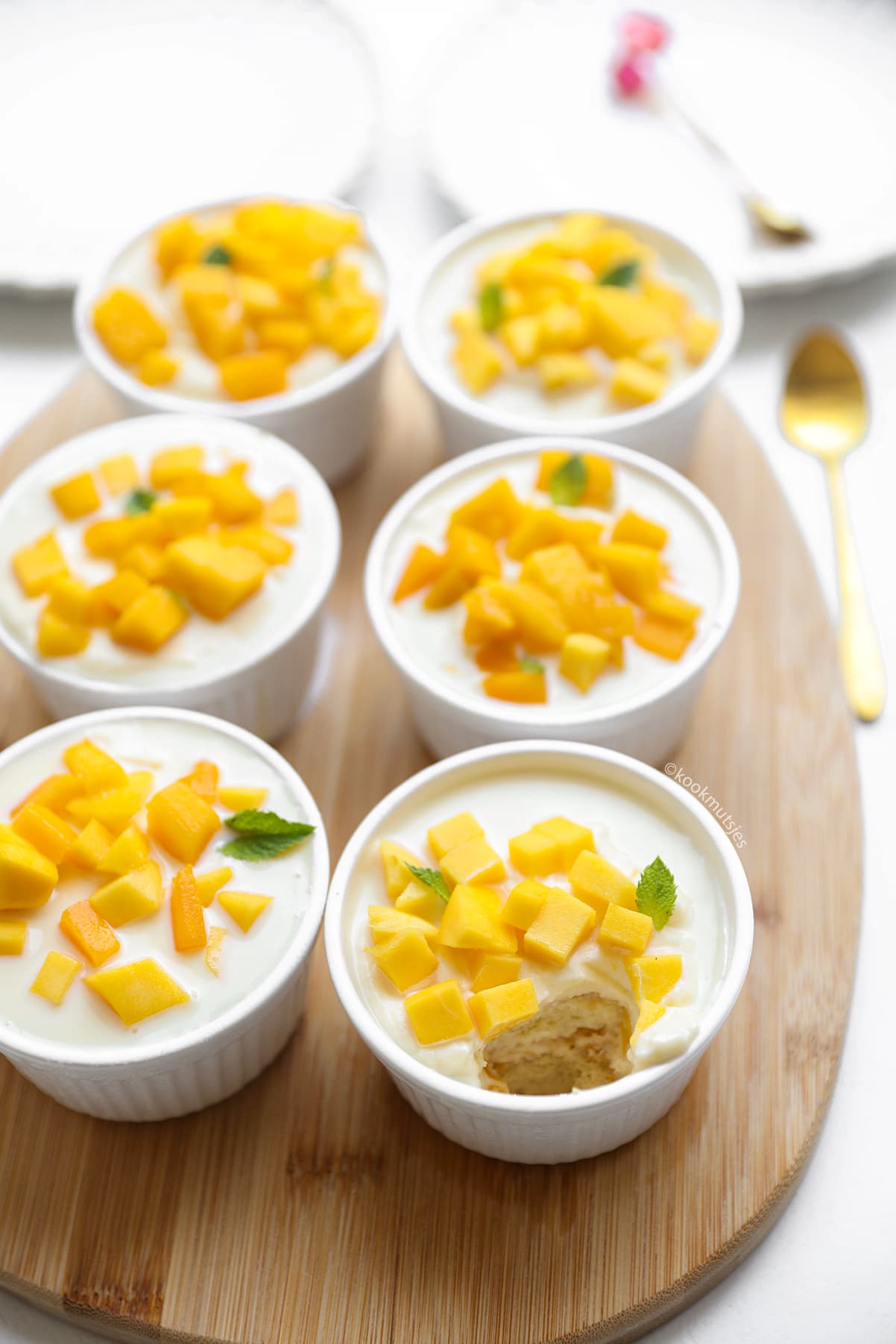 Mango tiramisu in glas met een hap eruit waardoor de laagjes mascarponeroom, mango en lange vingers zichtbaar zijn.