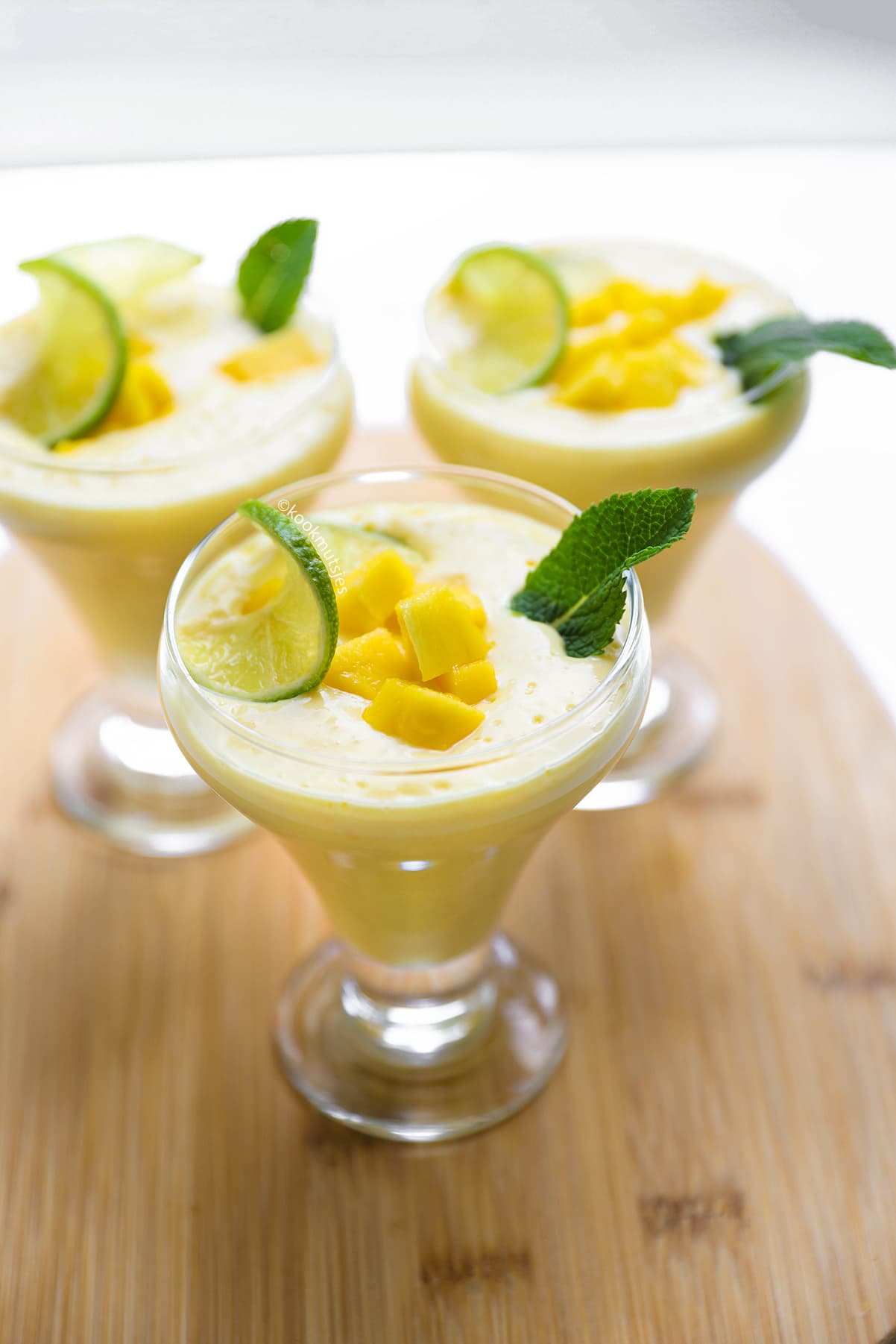 Twee glazen zelfgemaakte mango lassi, gegarneerd met verse mango, munt en limoen.
