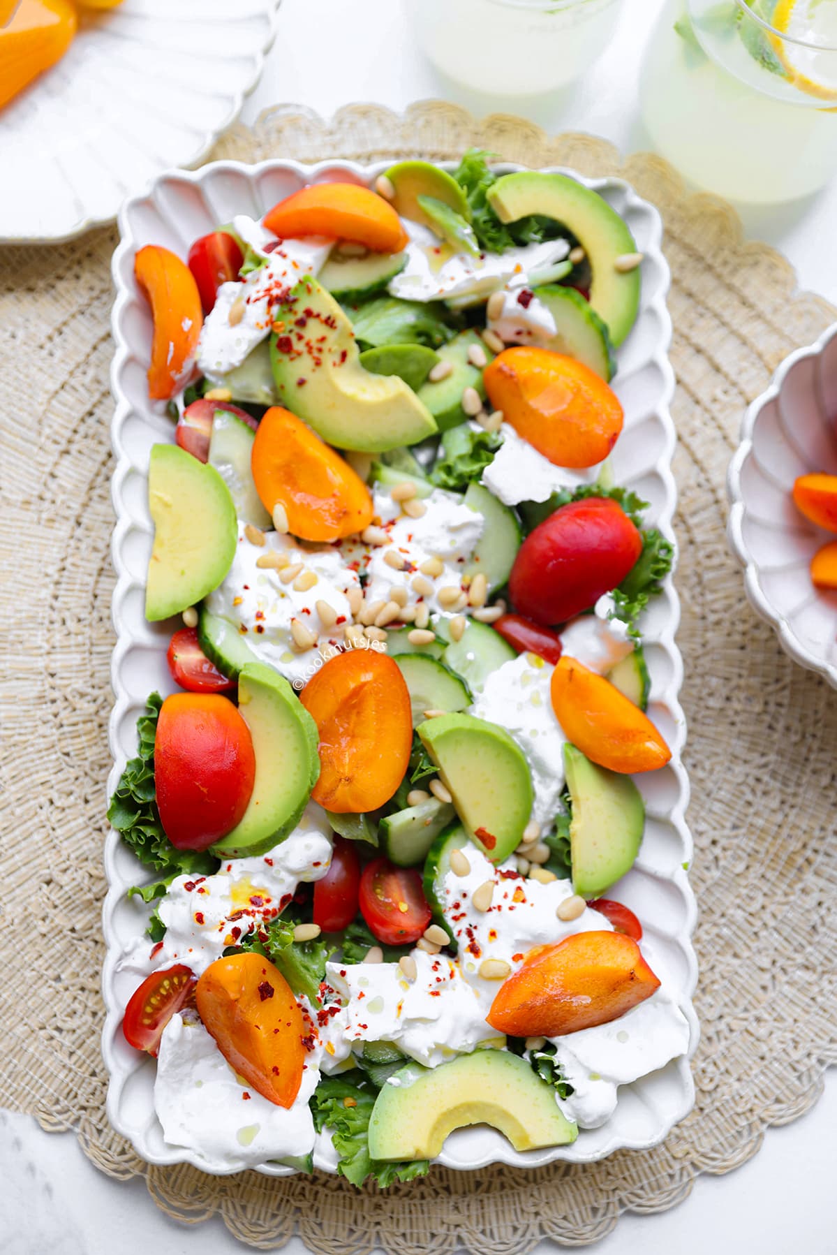 Kleurrijke zomerse salade met burrata, perzik, avocado, tomaat, komkommer en pijnboompitten.