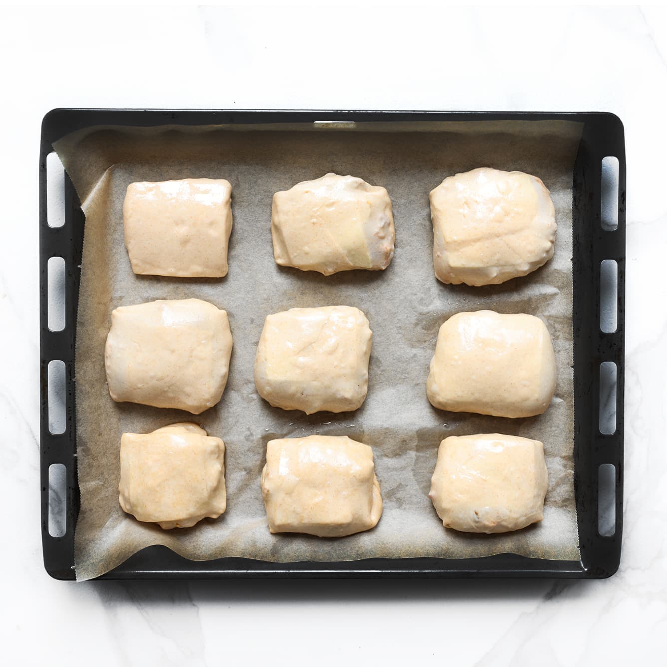 De gevulde kip pakketjes liggen met de naad naar beneden op een bakplaat.