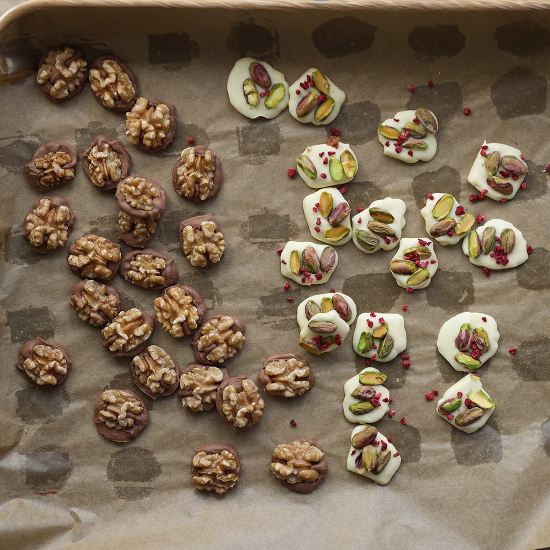 Zelfgemaakte chocolade flikken met noten en gevriesdroogde frambozen die uitharden op bakpapier.
