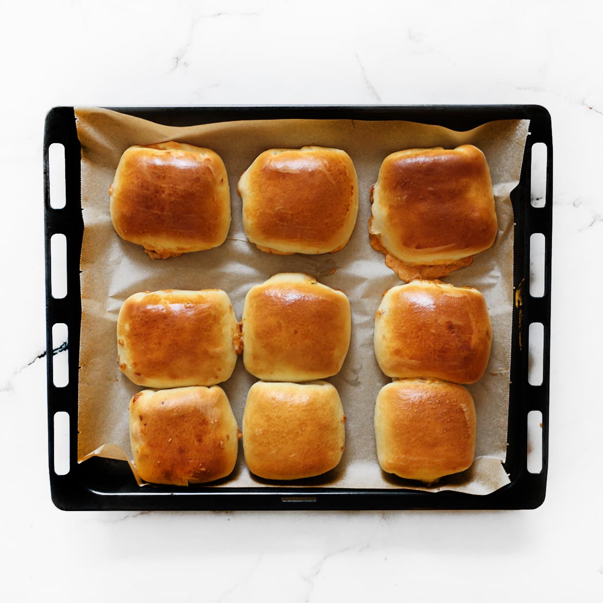 Goudbruine buffalo chicken broodjes versgebakken op een met bakpapier beklede bakplaat