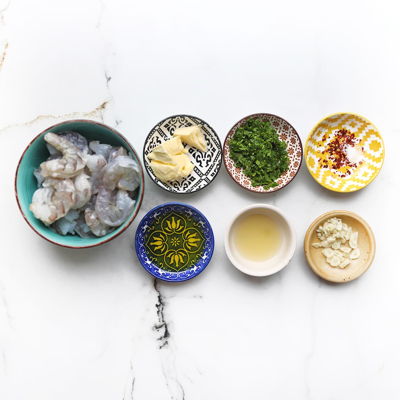 Ingrediënten voor knoflookgarnalen met gepelde garnalen, knoflook, peterselie, citroen en roomboter.